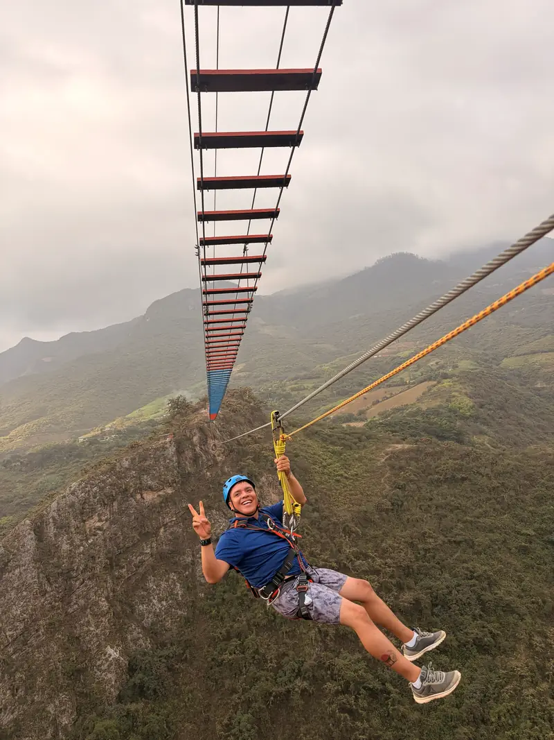 Visitante deslizándose en canopy sobre el valle de Tocmoche y haciendo la señal de victoria