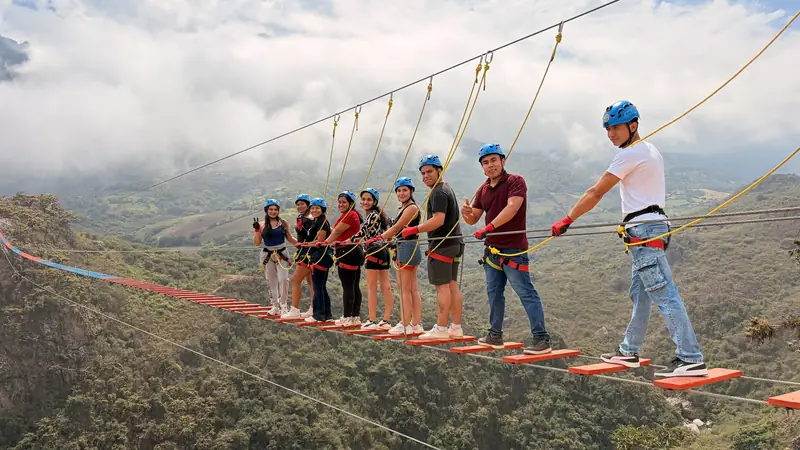 Grupo cruzando el puente tibetano con cascos azules y el valle al fondo