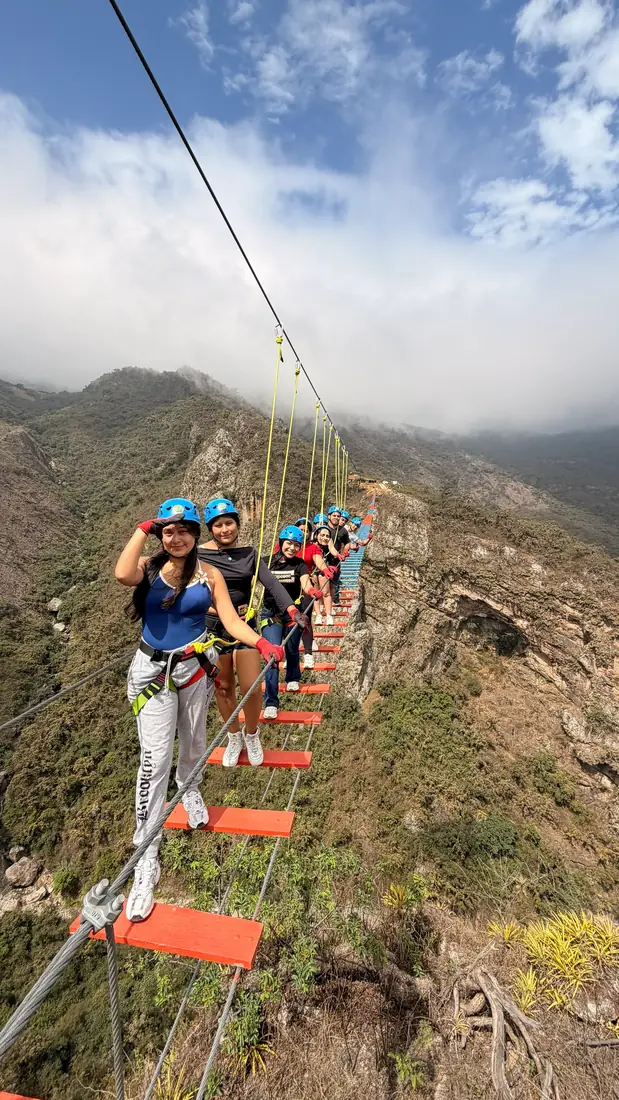 Grupo cruzando el puente colgante bajo un cielo azul con nubes
