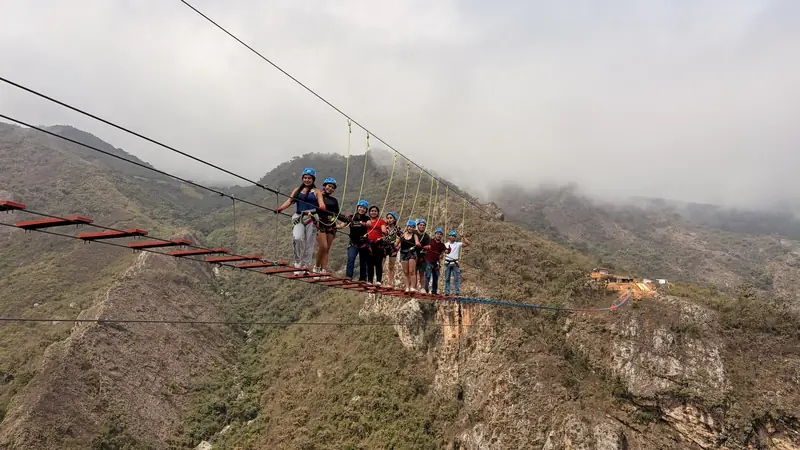 Vista lejana del puente tibetano con un grupo cruzándolo sobre la quebrada