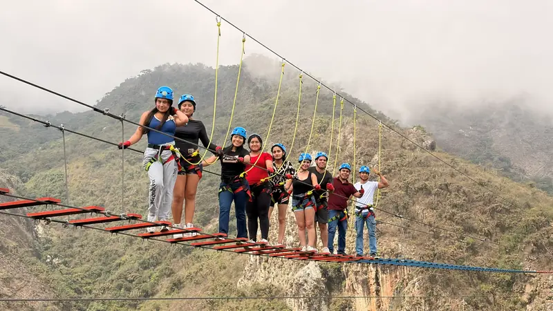 Viajeros sujetos a la línea de vida en el puente colgante, con niebla en las montañas