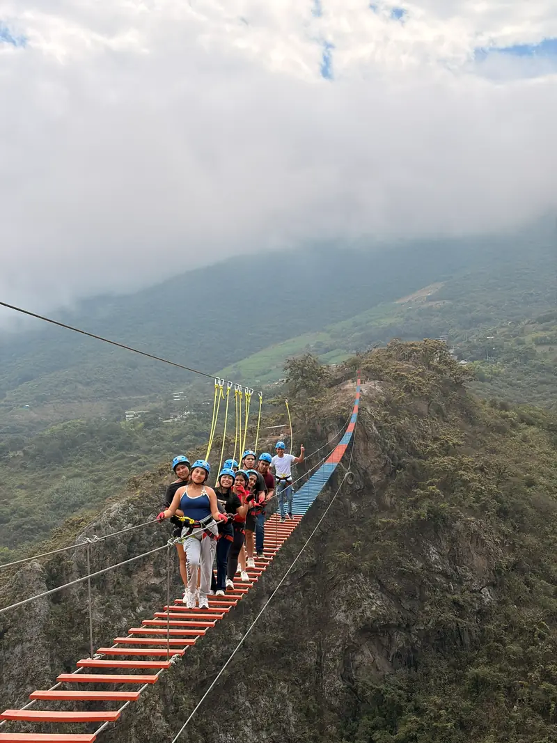 Grupo entrando al puente tibetano visto desde el extremo, con el cerro verde de fondo
