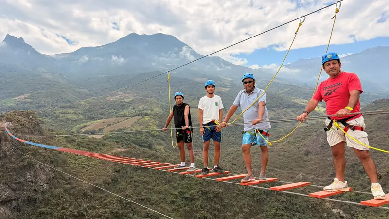 Guía sujetando la cuerda mientras cuatro viajeros cruzan el puente