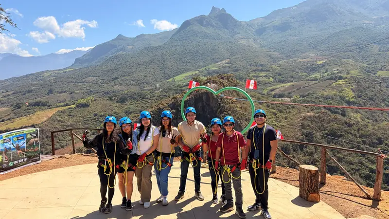 Grupo de viajeros con arnés y casco posando junto al corazón verde y las banderas del Perú en el mirador de Tocmoche