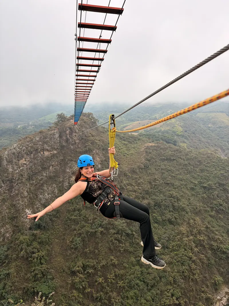 Viajera cruzando el canopy con los brazos abiertos sobre las montañas