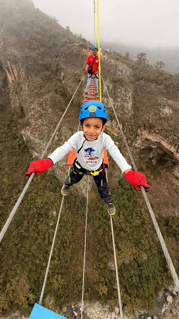 Niño con guantes rojos disfrutando del canopy sujeto al arnés
