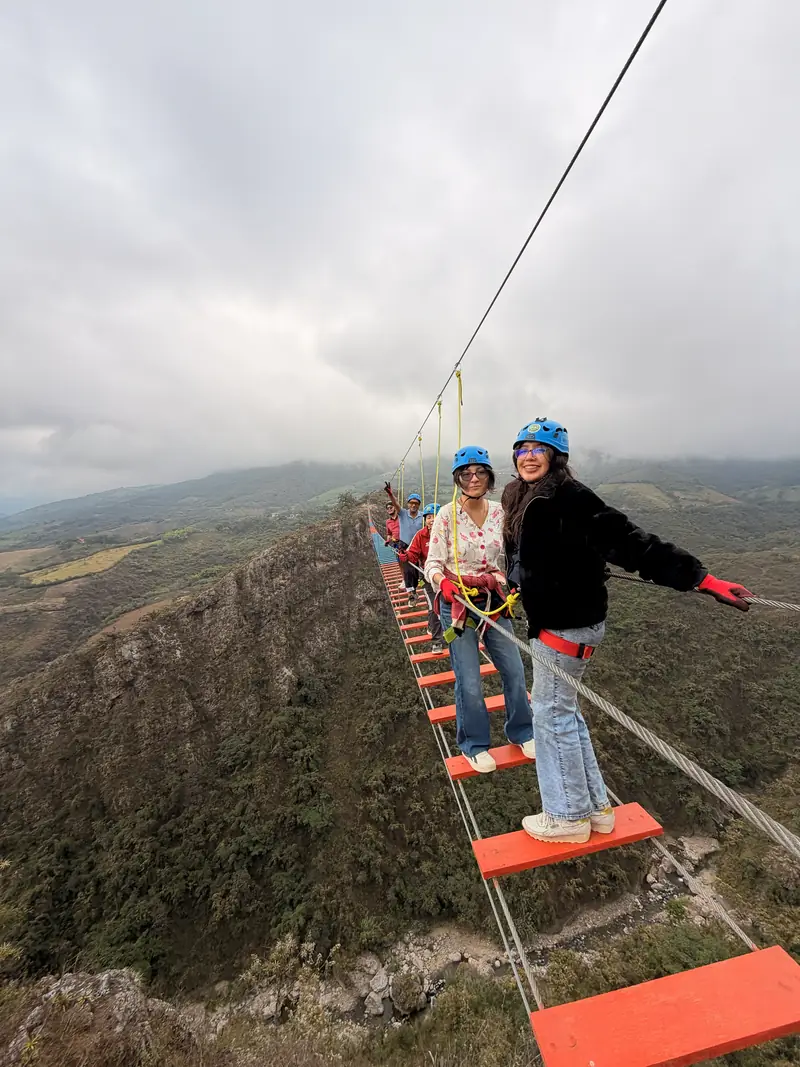 Dos viajeras cruzando el puente tibetano con los brazos abiertos