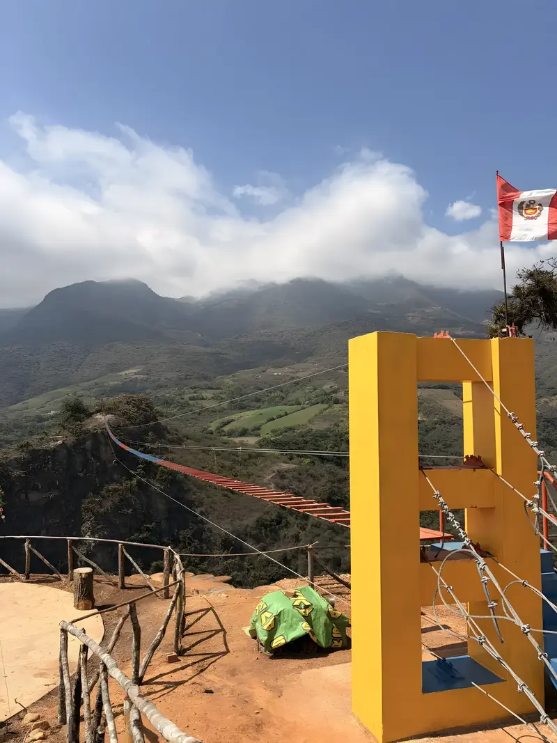 Mirador con el arco amarillo y la bandera del Perú, con el puente tibetano al fondo
