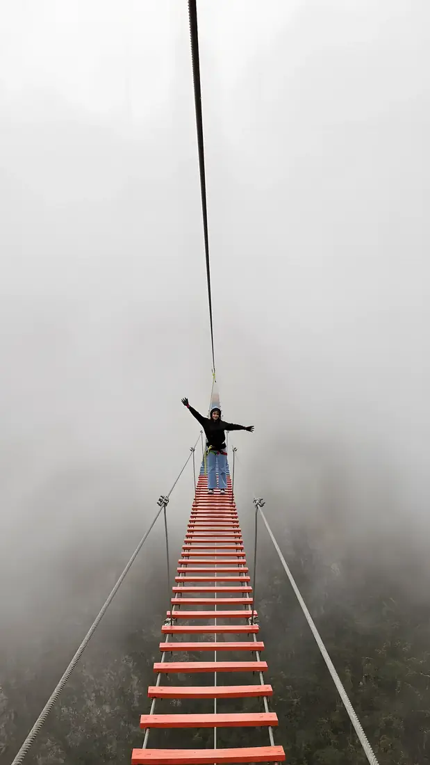 Viajera cruzando el puente tibetano entre la niebla con los brazos abiertos